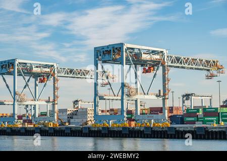 Boston, ma, États-Unis-8 décembre 2023 : grandes grues de chargement dans le port prêtes à charger des conteneurs d'expédition sur des navires avec des avions commerciaux volant au-dessus. Banque D'Images