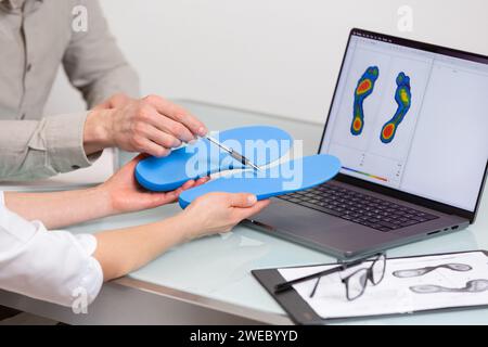 Femme médecin orthopédiste donne des consultations personnalisées de semelles intérieures à un patient masculin dans une clinique. Concept de récréation des pieds et de médecine orthétique Banque D'Images