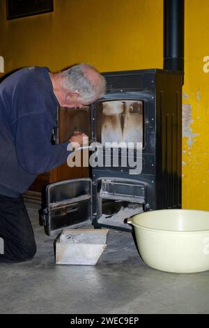 homme âgé mûr nettoyant le verre dans la porte sur le brûleur à bois domestique Banque D'Images