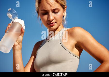 Maintenir l'hydratation. Une femme boit de l'eau pendant une séance d'entraînement, reconstituant son équilibre eau-sel, belle lumière, une femme étanche sa soif sur un s. Banque D'Images