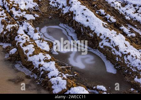 Eau gelée idyllique sur les chenilles de tracteur dans un champ avec des mottes de terre au soleil en hiver Banque D'Images