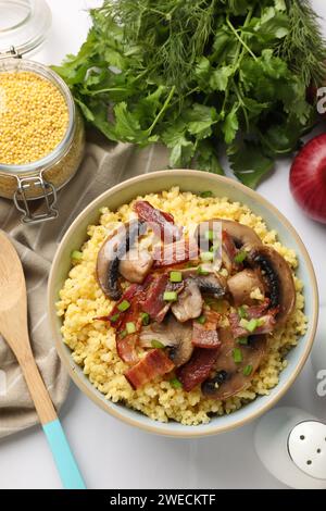 Bouillie de millet savoureuse avec champignons, bacon et oignon vert dans un bol sur une table blanche, mise à plat Banque D'Images