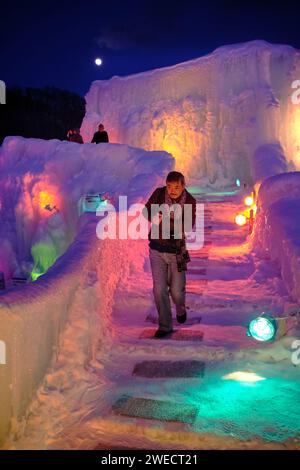 Chitose, Hokkaido, Japon - février 2018 : Homme marchant sur des marches de glace entourées de couleurs au Lake Shikotsu Ice Festival, un événement de sculpture de glace organisé dans les sources chaudes du lac Shikotsu dans le parc national Shikotsu-Toya avec des lumières illuminant des sculptures de glace mur de glace Banque D'Images