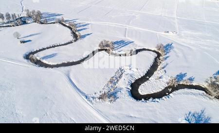 Drone shot de la rivière Schmutter serpentant naturellement à travers le paysage hivernal enneigé du parc naturel Western Forests près d'Augsbourg Banque D'Images