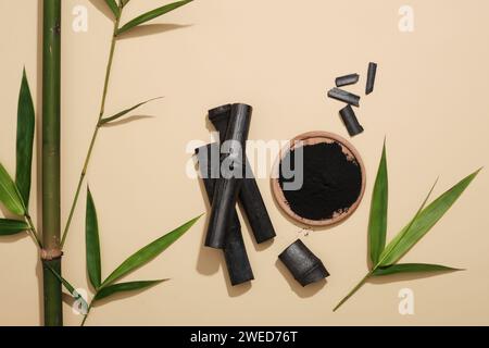 Un plat en bois de poudre de charbon de bambou activé décoré de bâtons de charbon actif et de feuilles vertes. Produit cosmétique organique Banque D'Images