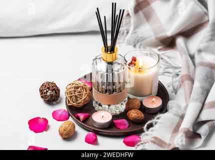 Ambiance chaleureuse de la maison. Parfum liquide maison dans une bouteille en verre et bougie parfumée sur plateau Banque D'Images