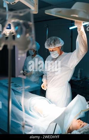 Tir vertical de l'opération chirurgicale par les chirurgiens professionnels. Médecin ajustant l'opération légère en portant une blouse médicale. Banque D'Images