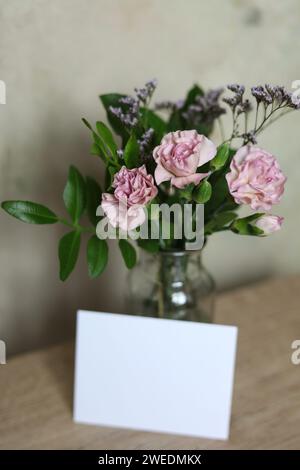 Bouquet de fleurs d'œillet rose dans un vase en verre avec une note vierge sur la table Banque D'Images