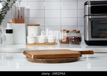 Empilés de planche à découper en bois forment un podium vide pour le produit d'affichage. En arrière-plan se trouve le comptoir avec des boîtes à épices, un plateau à couteaux et un micro-ondes Banque D'Images