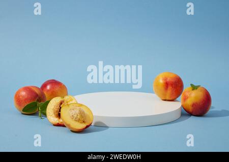 Piédestal pour les maquettes de produits cosmétiques et d'emballage présentation d'affichage - un podium blanc rond avec des pêches mûres (prunus persica) décorées sur un bleu Banque D'Images