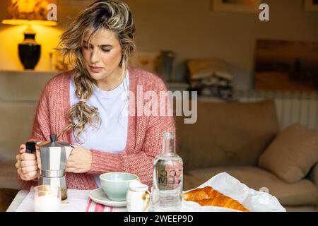 Un cadre de petit déjeuner intime avec une femme appréciant le plaisir simple de faire du café à l'aide d'un pot de moka, complété par un croissant frais. Banque D'Images