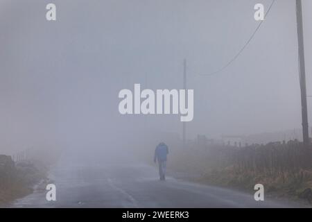 La brume sur une colline de Pennine près de Queensbury transforme les fermes et les marcheurs en silhouettes fantômes alors que le temps hivernal saisonnier de janvier se rapproche. Banque D'Images