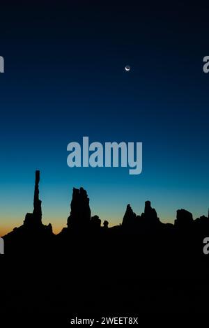 Lune au-dessus du Totem Pole et le Yei Bi Chei en silhouette avant l'aube dans le Monument Valley Navajo Tribal Park en Arizona. Banque D'Images