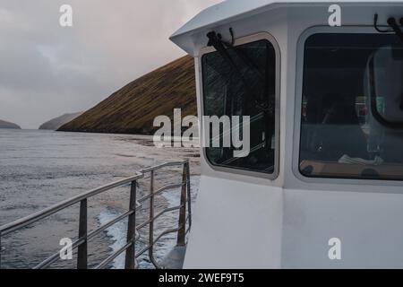 Un bateau naviguant le long d'un rivage rocheux pendant la journée, îles Féroé Banque D'Images