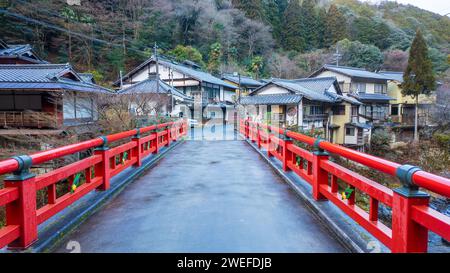 Étroit pont rouge mène à des maisons traditionnelles dans le village japonais Banque D'Images