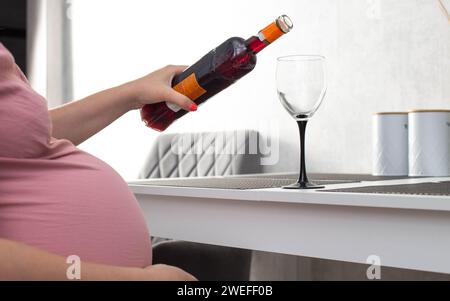 Une fille enceinte verse le vin d'une bouteille dans un verre. La notion de consommation d'alcool pendant la grossesse. Préjudice et troubles cognitifs chez l'enfant. ALC Banque D'Images