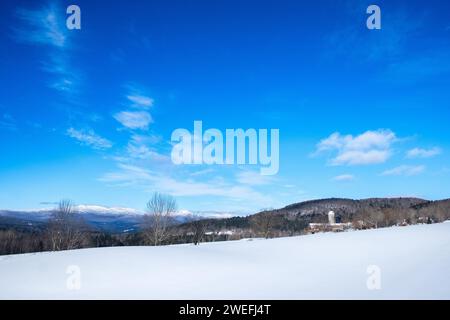 Une grange et un silo dans un champ enneigé à East Montpelier, Vermont, USA, à quelques kilomètres de Montpelier. Montagnes vertes enneigées au loin. Banque D'Images