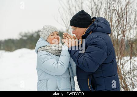 Un homme âgé et attentionné réchauffe les mains de sa femme avec son souffle dans la rue. Saint Valentin Banque D'Images