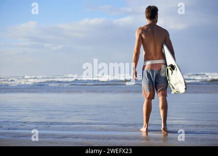 Surf, fitness et dos de l'homme à une plage avec planche de surf pour la liberté, les voyages ou le sport en plein air. Océan, entraînement et surfeur masculin à la mer pour Banque D'Images