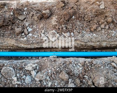 Le nouveau tuyau de PVC est posé dans la tranchée près de la route le long de béton pour le système d'approvisionnement en eau du village rural, vue de face avec la copie s Banque D'Images