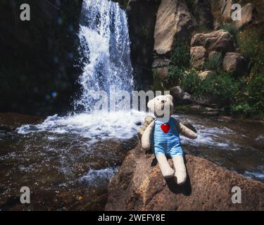 Peluche jouet ours en peluche voyageur assis sur un rocher à la cascade de la rivière en vacances dans la gorge de Kaskasu en été Banque D'Images