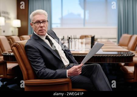 Homme d'affaires senior posant dans un fauteuil avec des documents dans ses mains et regardant avec confiance la caméra Banque D'Images