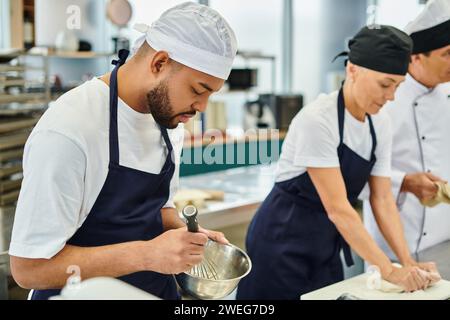 concentrez-vous sur le chef afro-américain fouettant les ingrédients à côté de son collègue flou et chef cuisinier Banque D'Images