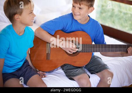 Enfants, musique et frères et sœurs sur un lit avec guitare pour jouer, se lier ou apprendre ensemble dans leur maison. Instrument de musique, amour et enfants Banque D'Images