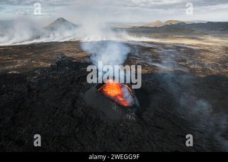 Éruption volcanique en Islande, cratère sommital, expulsion de gaz, et lave fondue se déversant d'un évent, vue latérale aérienne. Risques naturels et géothermie Banque D'Images