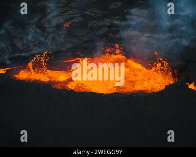 Éruption volcanique en Islande, cratère sommital, expulsion de gaz, et lave fondue se déversant d'un évent, vue latérale aérienne. Risques naturels et géothermie Banque D'Images