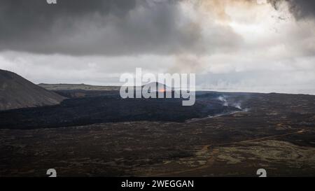 Éruption volcanique en Islande, une fontaine de lave rouge incandescente s'élevant au-dessus d'un évent et une coulée de lave s'étendant rapidement en descente, tir aérien. Banque D'Images