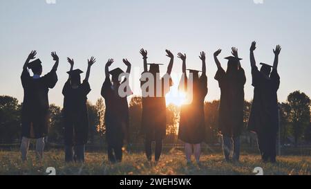 Diplômés de l'université en robes ondulant au coucher du soleil. Banque D'Images