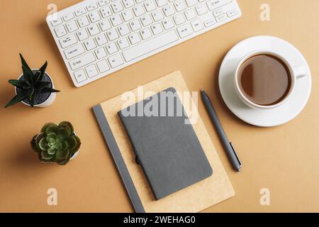 Bureau avec bloc-notes, clavier, tasse à café et plantes succulentes sur table beige. Vue de dessus, pose à plat. Banque D'Images
