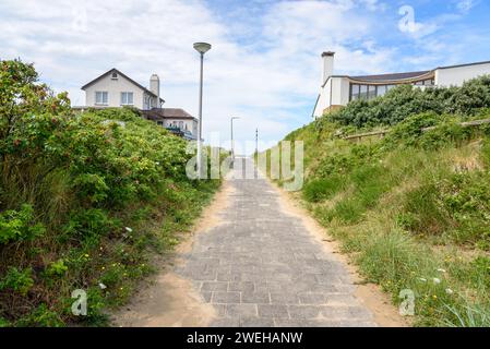 Sentier vide entre deux maisons modernes menant à une plage sur une journée d'été partiellement nuageuse Banque D'Images