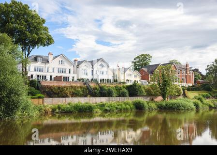 Rangée de maisons modernes sur la rive d'une rivière par une journée d'été partiellement nuageuse Banque D'Images