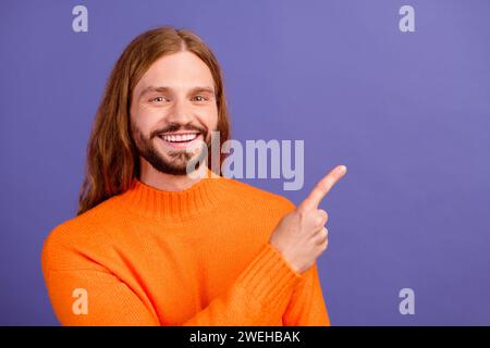 Portrait de jeune homme beau blond à cheveux longs portant orange pull tendance nouveauté doigt direct isolé sur fond de couleur violette Banque D'Images