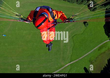 Un homme en salopette rouge signal pend d'un parapente au-dessus des prairies près de Lenggries, perspective du pilote, Bavière, Allemagne, Europe Banque D'Images