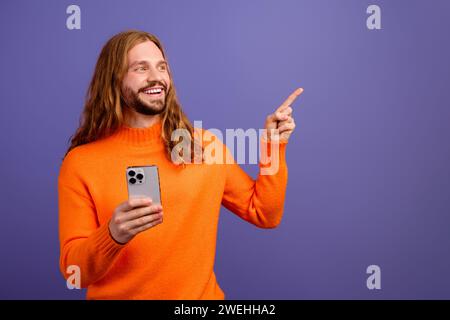 Photo de gars curieux porter un pull orange avec iphone touriste en utilisant google maps point doigt meilleurs endroits isolés sur fond de couleur violette Banque D'Images