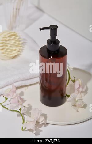 Une bouteille ambre sans étiquette avec buse de pompe, maquette pour produit de soin capillaire sur plateau rond, fleurs, brosse de massage du cuir chevelu et serviette en coton décorée sur whit Banque D'Images