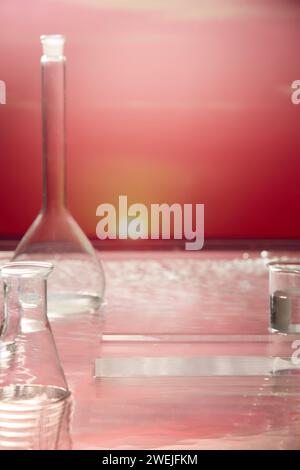 Scène pour la publicité de produit cosmétique avec concept de laboratoire. Équipement de laboratoire et podium transparent décoré sur l'eau et le fond rose du ciel de coucher de soleil Banque D'Images