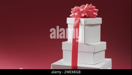 Trois boîtes-cadeaux empilées attachées avec un ruban rose, placées sur un fond rouge Banque D'Images