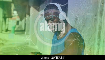 Scanner rond contre un homme afro-américain en forme portant un casque utilisant une smartwatch à l'extérieur Banque D'Images