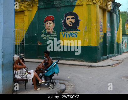 Femmes cubaines socialisant près d'un bâtiment peint avec les portraits de Hugo Chávez et Che Guevara dans la vieille Havane, Cuba. Banque D'Images