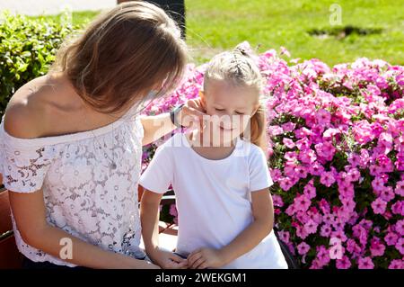 Mère et fille assises sur un banc dans le parc de la ville d'été. Enfance, loisirs et concept de personnes - repos familial heureux et passer un bon moment Banque D'Images