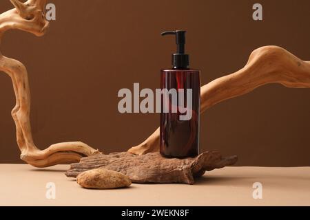 Scène avec bouteille ambre sans étiquette et brindilles séchées décorées sur fond brun. Récipient en plastique vierge pour cosmétiques pour crème, lotion ou shampooing. B Banque D'Images