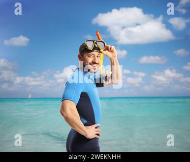 Jeune homme en combinaison de plongée et masque marchant dans une mer bleue cristalline Banque D'Images