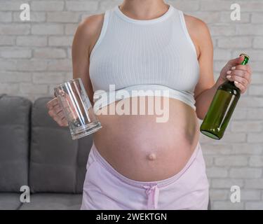 Femme enceinte tenant verre et bouteille de bière. Banque D'Images