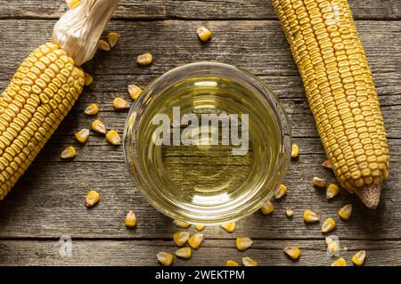 Huile de maïs dans un bol avec des gruaux de maïs séchés et des grains sur fond rustique. Composition d'huile de cuisson Banque D'Images