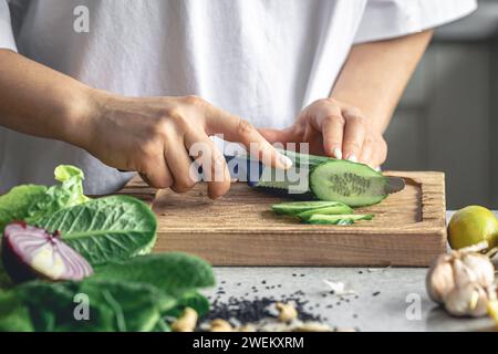 Une femme coupe un concombre frais sur une planche de bois dans la cuisine. Banque D'Images