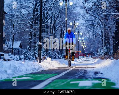 Un homme satisfait, souriant et barbu fait du vélo en hiver dans la ville le long d'une piste cyclable tard dans la nuit. Mode de vie actif en ville. Une vie saine Banque D'Images